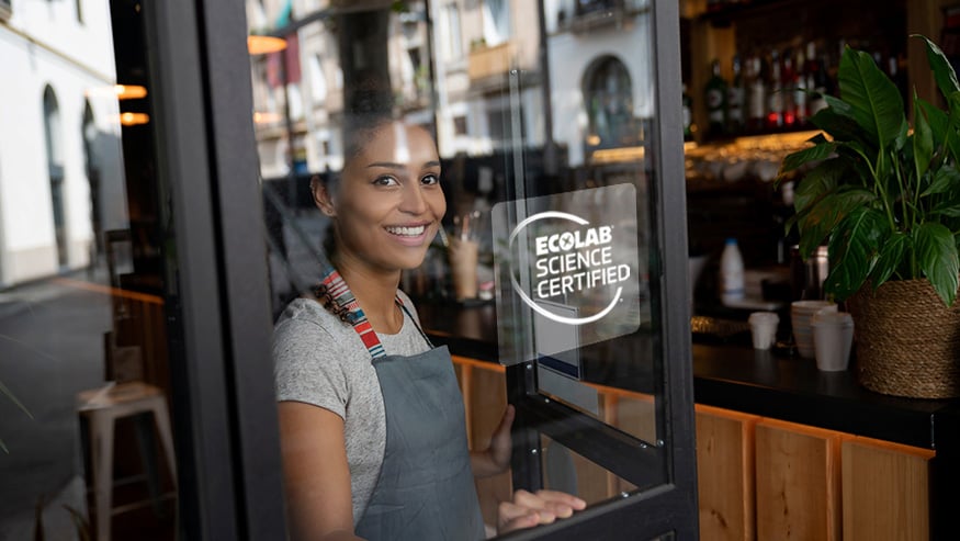 Restaurant worker smiling and standing behind a glass door that has the ESC logo on it