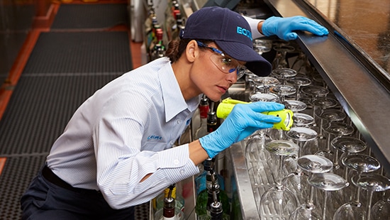 Ecolab pest control specialist with protective equipment and a flashlight inspecting the back of a bar