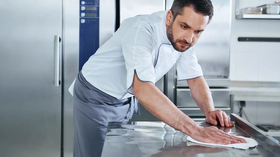 A photo of a person cleaning an institutional kitchen
